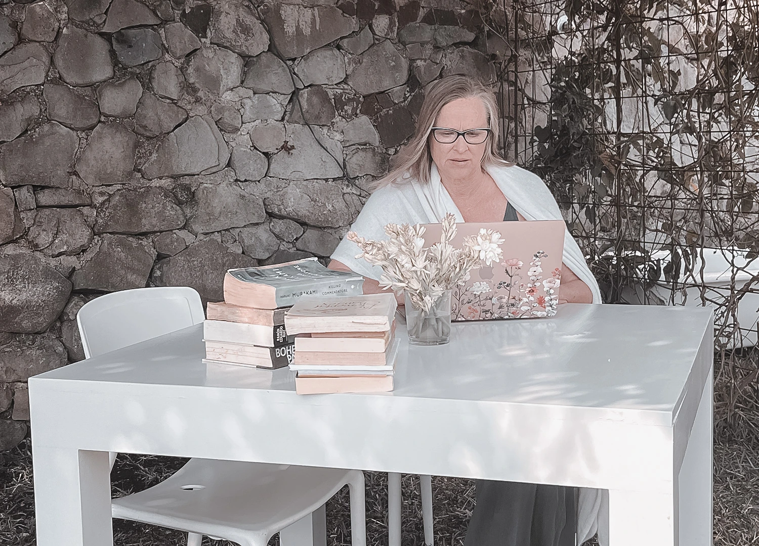 A woman working on a laptop beside a stack of books