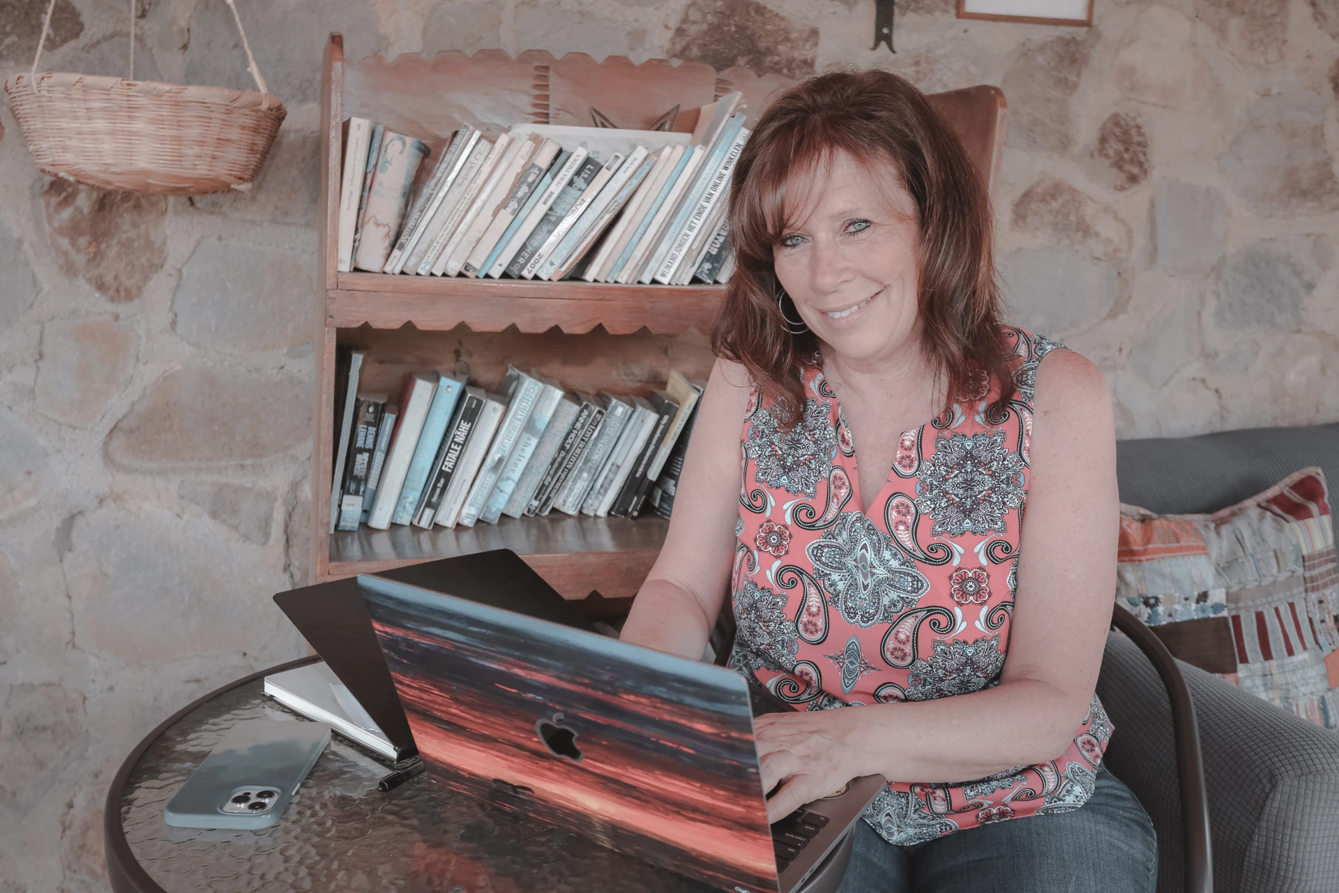 A woman working on a laptop beside a bookshelf.